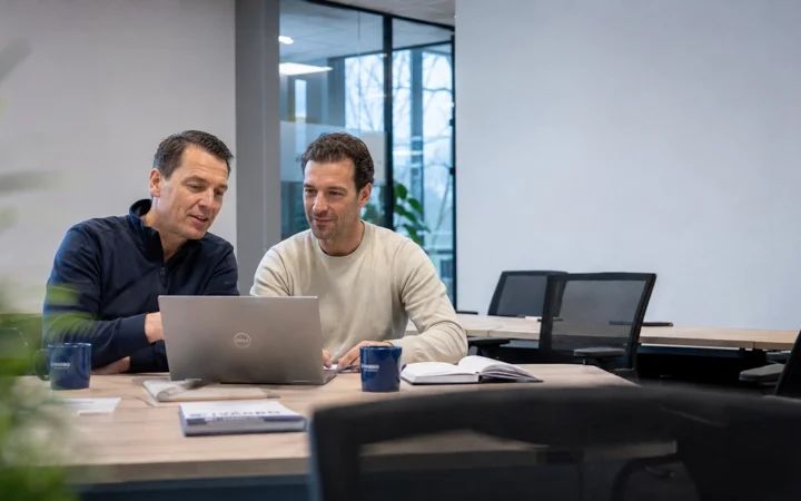 Kandidaat bereidt zich met laptop voor op een VCA proefexamen terwijl een adviseur uitleg geeft.